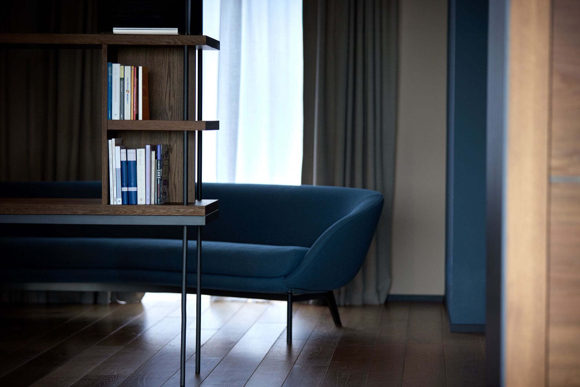 Uma sala de estar moderna com um sofá azul, uma estante de madeira e uma mesa de centro de vidro.