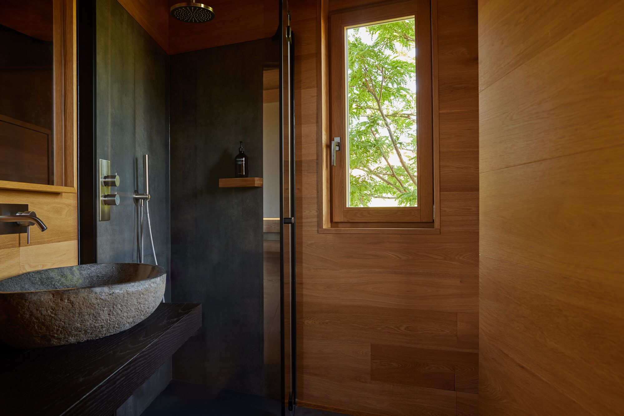 A bathroom with a stone sink, a shower, and a wooden door with a window.