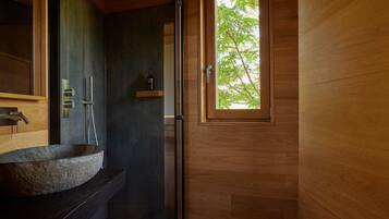 A bathroom with a stone sink, a shower, and a wooden door with a window.