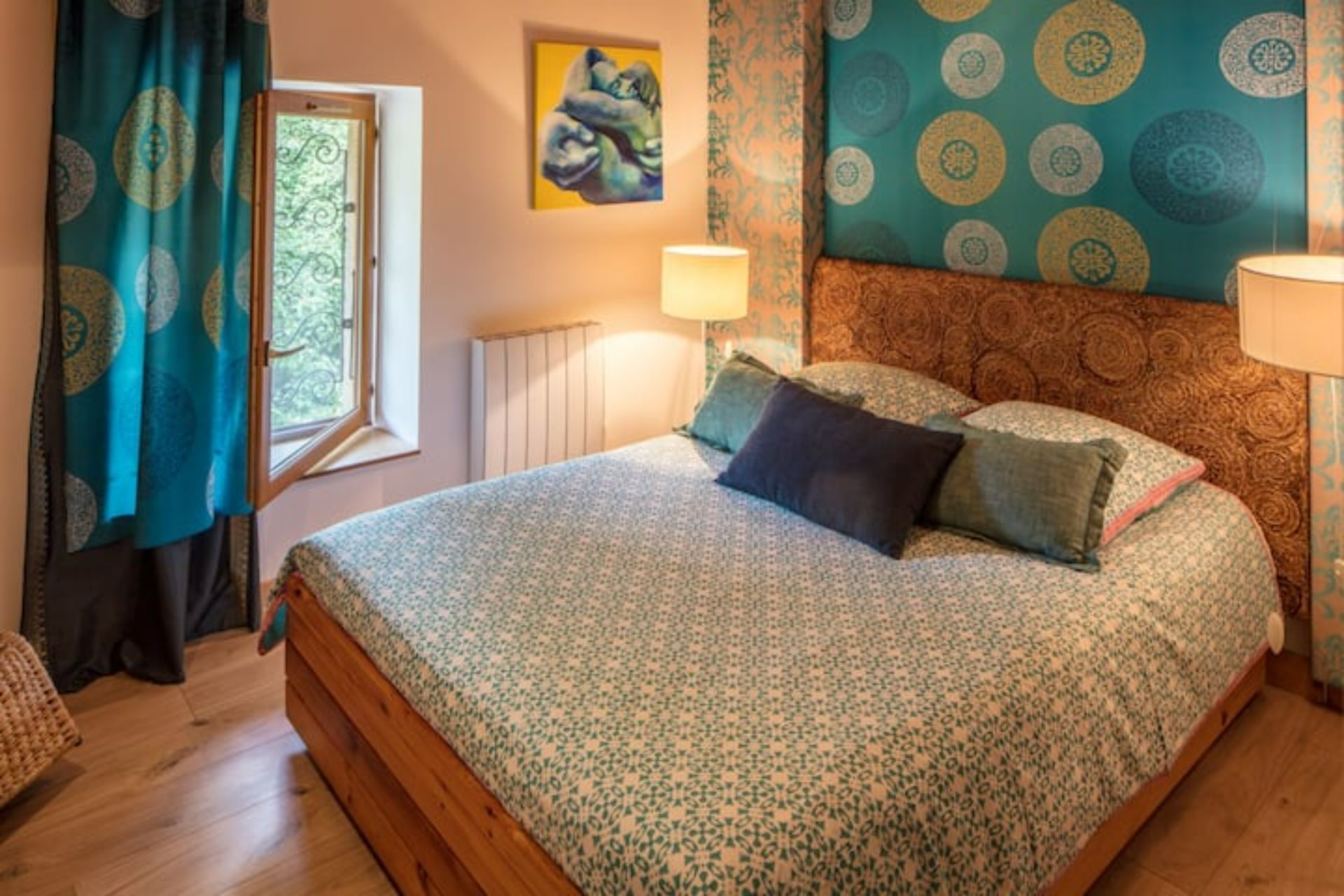 A bedroom with a large bed, patterned curtains, a radiator, and a painting on the wall.