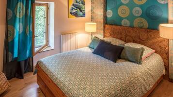 A bedroom with a large bed, patterned curtains, a radiator, and a painting on the wall.