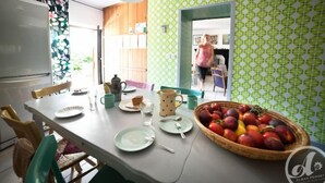 A dining area with a table set for two, a basket of fruit, and a kitchen in the background. - Artist'au Chat" family gîte with sauna (saint paul)