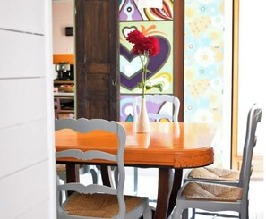 A dining area with a wooden table, two chairs, and a vase with red flowers.