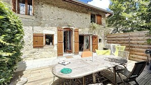 A rustic stone building with wooden shutters, a wooden deck, and a table with chairs. - Artist'au Chat" family gîte with sauna (saint paul)