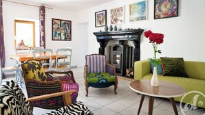 A living room with a dining area, a fireplace, and various artworks on the walls. - Artist'au Chat" family gîte with sauna (saint paul)