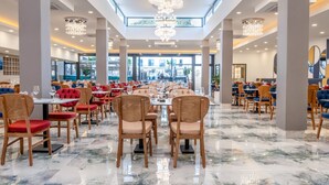 A spacious dining area with multiple tables and chairs, large chandeliers, and a view of the outside through large windows. - Saint Star Kemer (Kemer)