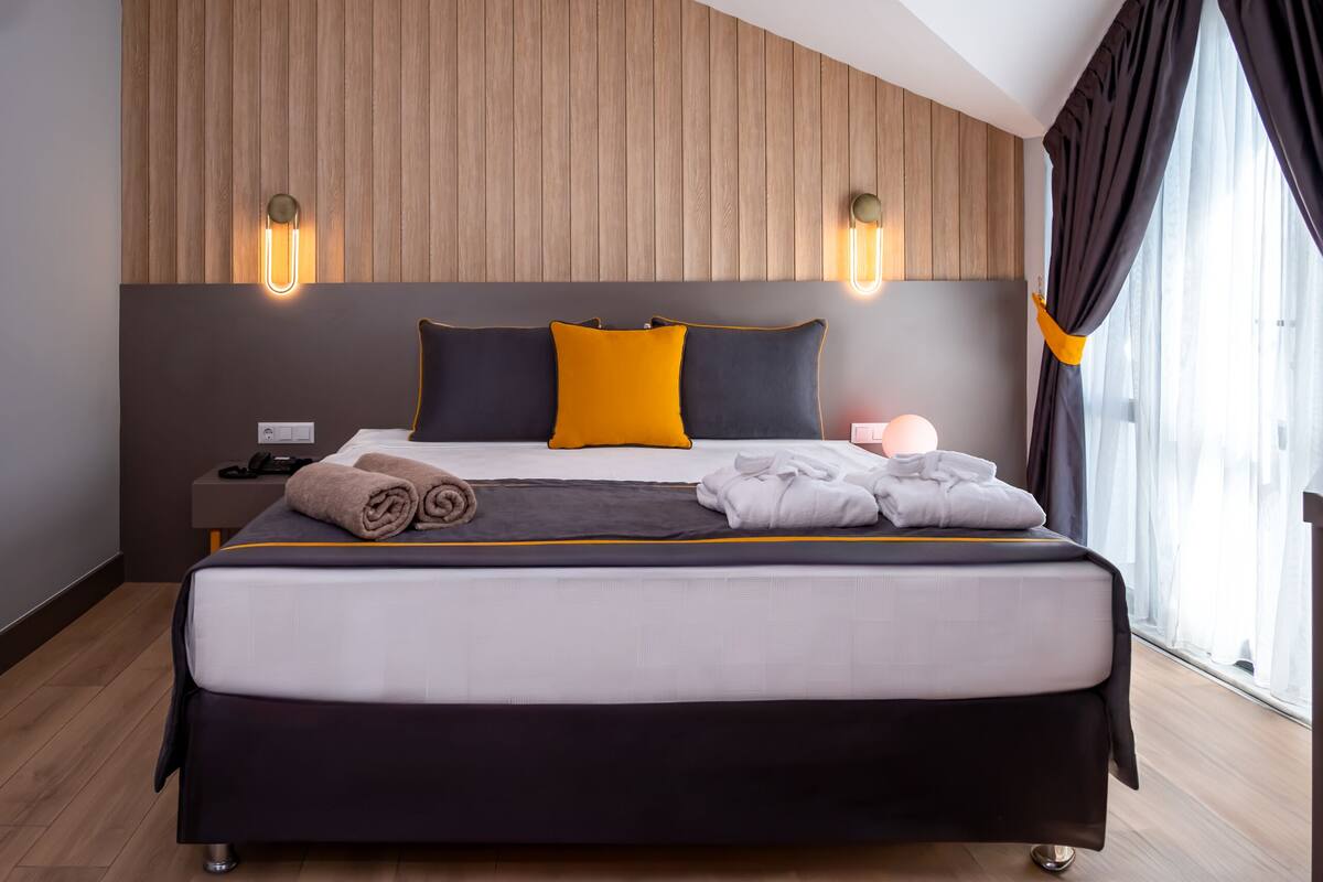 A modern hotel room with a large bed, wooden panel wall, and two bedside lamps.