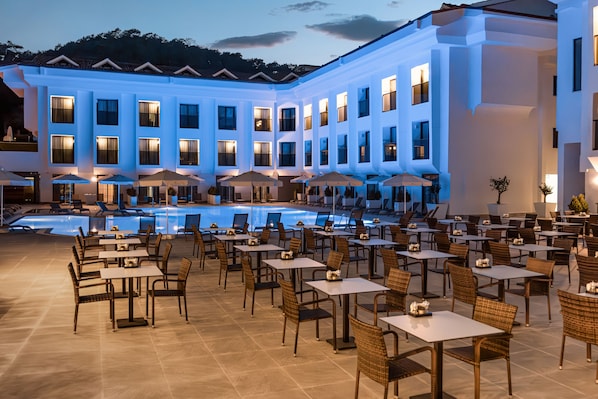 Um hotel com piscina, área de estar externa com guarda-sóis e um edifício grande com várias janelas.
