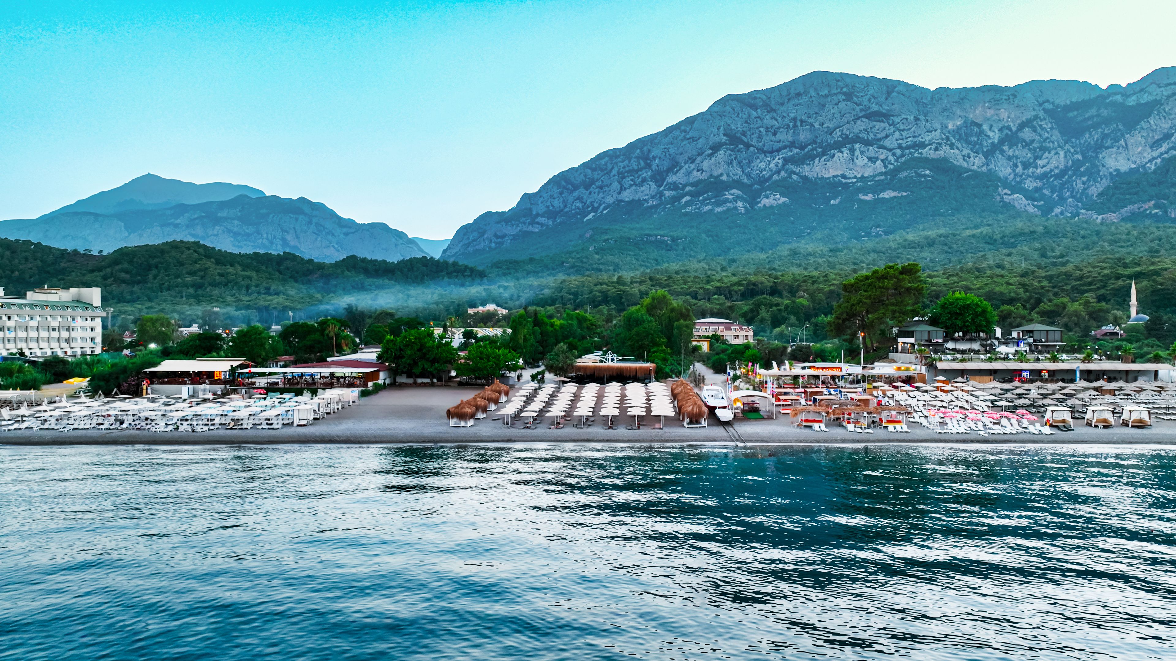 A coastal resort with beachside seating, a marina, and mountainous backdrop.