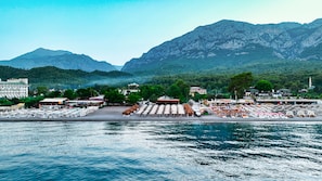 Resort costeiro com assentos à beira-mar, marina e montanhas ao fundo.