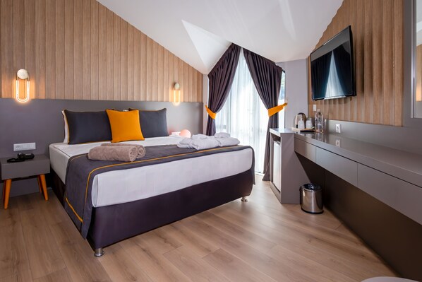 A modern hotel room with a large bed, wooden panel walls, a flat-screen TV, and a small kitchenette. - Saint Star Kemer (Kemer)