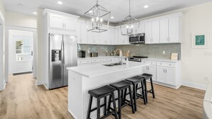 Una cocina moderna con armarios blancos, electrodomésticos de acero inoxidable y una isla central con taburetes de bar.