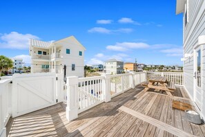 A wooden deck with a picnic table, white railings, and a view of neighboring buildings. - Watercolor-Mexico Beach! Gulf-Side Home! (Mexico Beach)