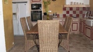 A dining area with wicker chairs and a table, a kitchen with red and white checkered tiles, and a refrigerator. - Gîte le plane tree (Aubignan)