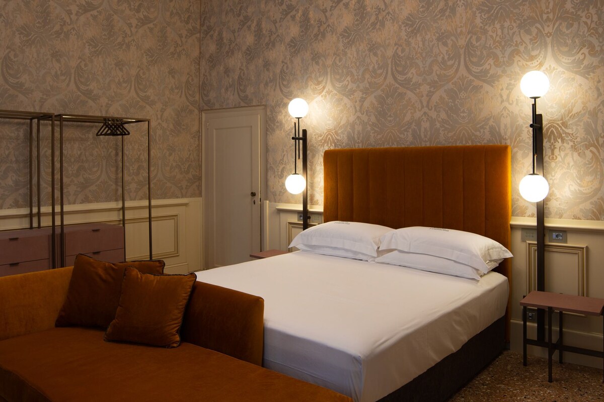A hotel room with a large bed, two bedside tables, a wardrobe, and a mirror.