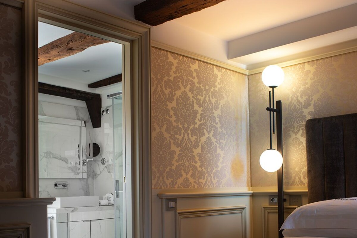 Habitación de hotel con una cama, una mesita de noche, un espejo y un baño visible a través de una puerta abierta.