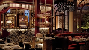 A bar area with a marble countertop, shelves of bottles, and a seating area with red upholstered chairs and tables. - Eight Venezia (Venice)