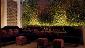 A cozy seating area with plush sofas and ottomans, a round table with a bottle and glasses, and a wall adorned with green foliage. - Eight Venezia (Venice)