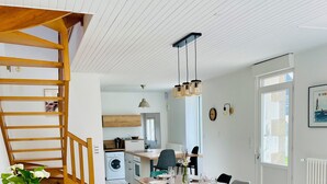 Uma cozinha moderna com escada de madeira, sala de jantar com mesa posta para quatro pessoas e um sofá amarelo na sala de estar.