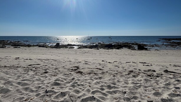 Uma praia com céu claro, mar calmo e costa rochosa.