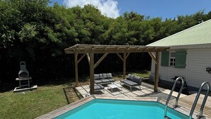 A swimming pool with a wooden deck and a covered seating area. - VILLA KAZ’ARY (Sainte-Anne)