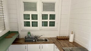 A compact kitchen with a sink, a washing machine, and a small stool. - VILLA KAZ’ARY (Sainte-Anne)