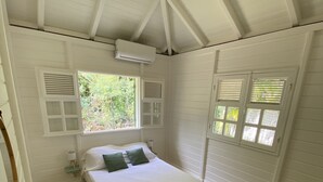 A bedroom with a bed, two windows with shutters, a ceiling fan, and a small bedside table with a lamp. - VILLA KAZ’ARY (Sainte-Anne)
