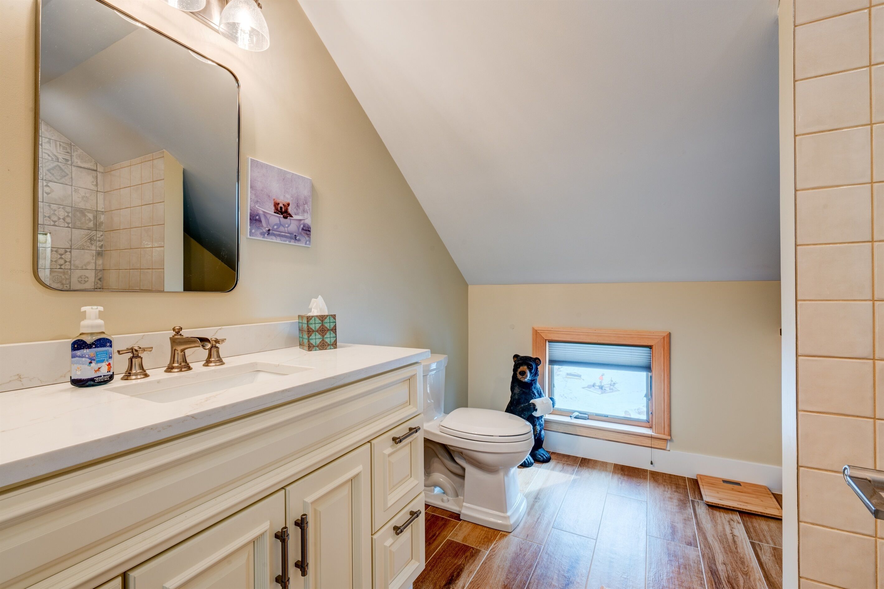 Une salle de bain avec un meuble-lavabo blanc, un grand miroir, des toilettes et une petite fenêtre.
