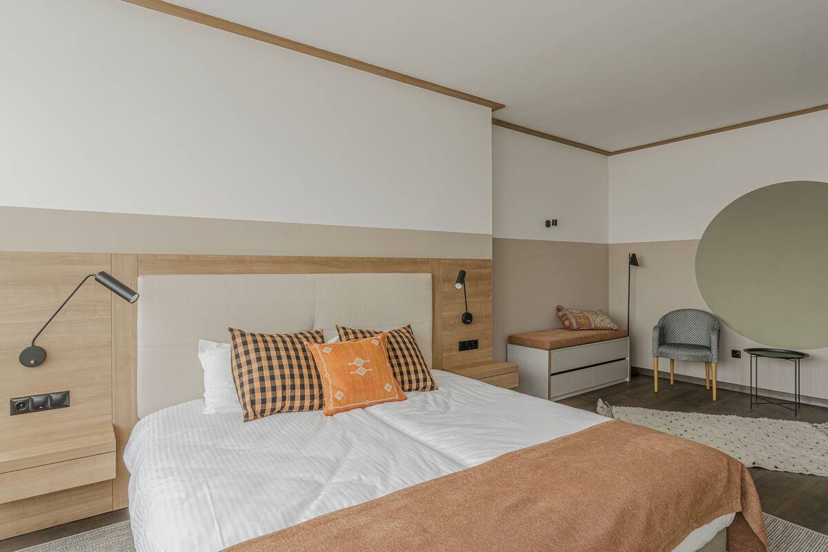 A modern bedroom with a large bed, a bedside table, a chair, and a round mirror.
