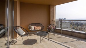 A balcony with two chairs and a small table, a glass door, and a city view.