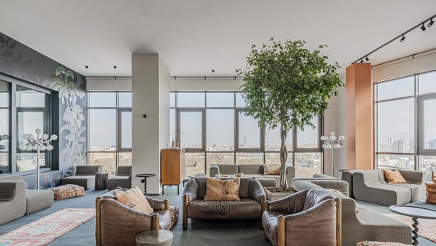 A spacious living area with multiple seating options, a large window offering a city view, and a central plant. -  WorkNomads LAB Hotel-Coliving & Coworking (Sofia)