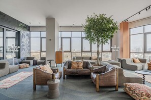 A spacious living area with multiple seating options, a large window offering a city view, and a central plant.
