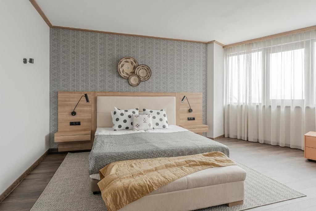 A bedroom with a bed, bedside tables, a wall-mounted clock, and a window with curtains.