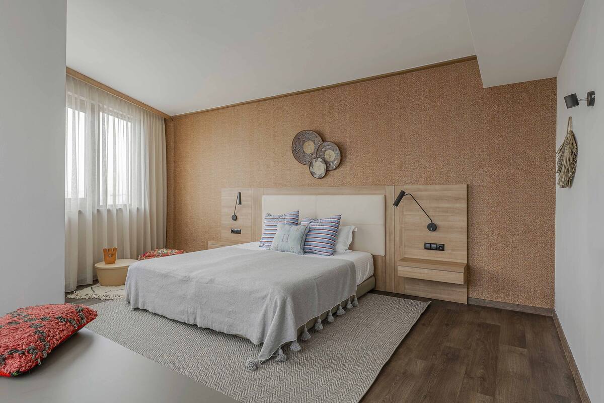 A modern bedroom with a large bed, a bedside table, a wall-mounted lamp, and a decorative wall piece.