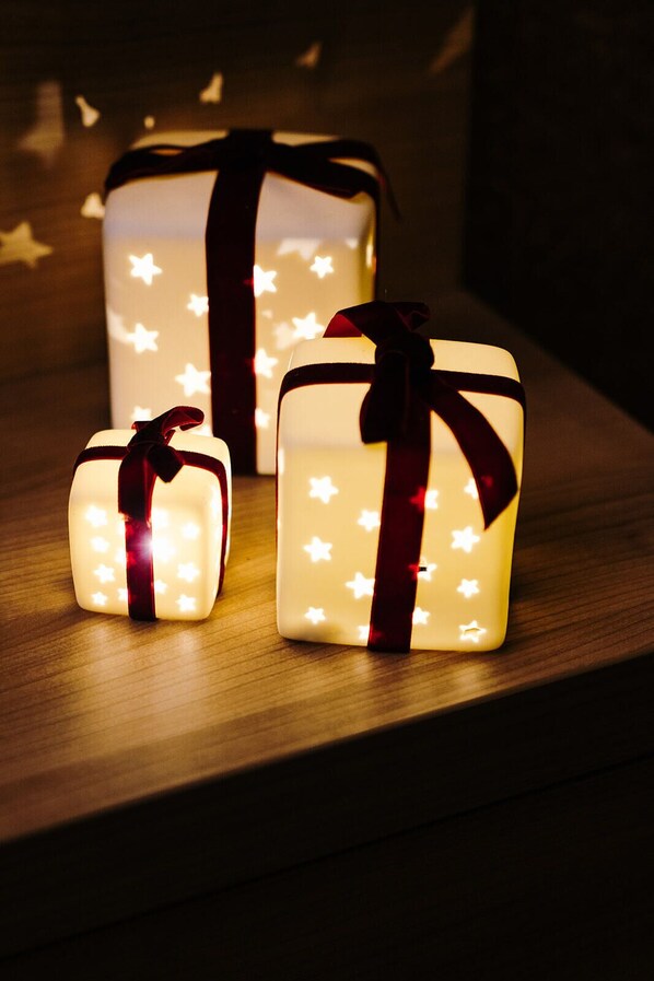 Three illuminated gift boxes with star patterns and red ribbons on a wooden surface.