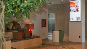 A hotel lobby with a seating area, a patterned rug, and a digital display advertising room rates.