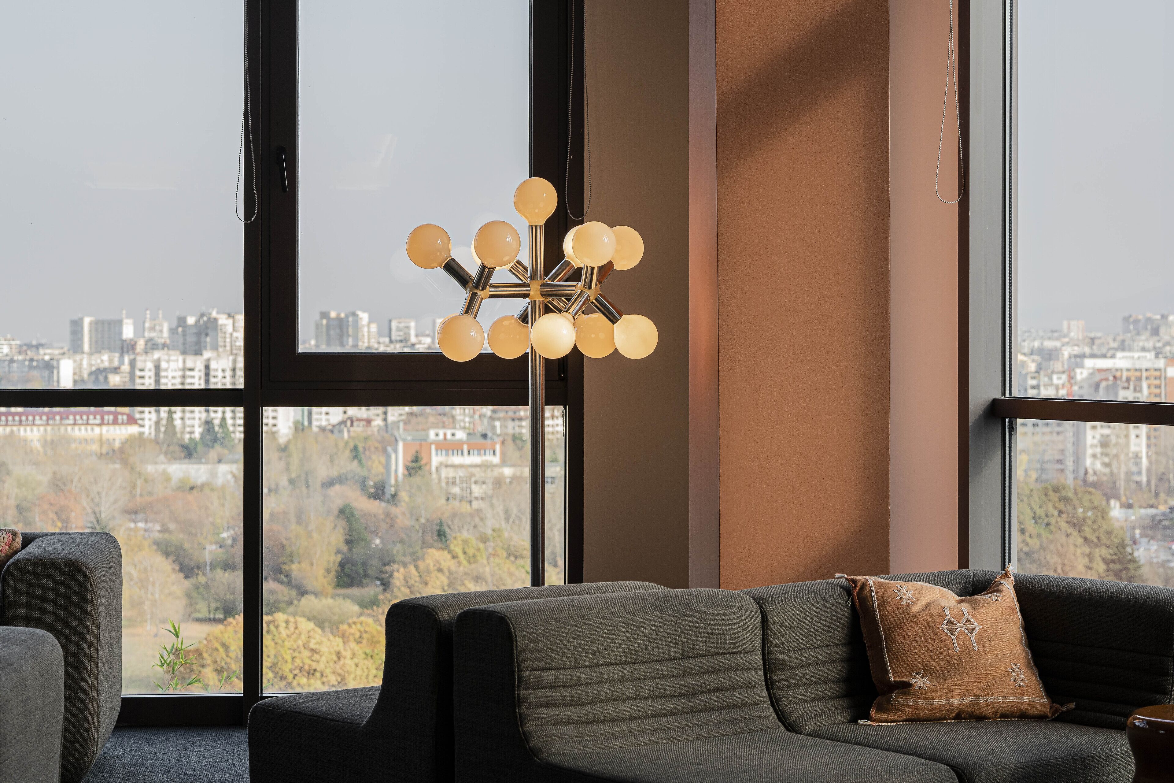 En moderne stue med et stort vindue, en moderne gulvlampe og en sofa med et dekorativt pude.