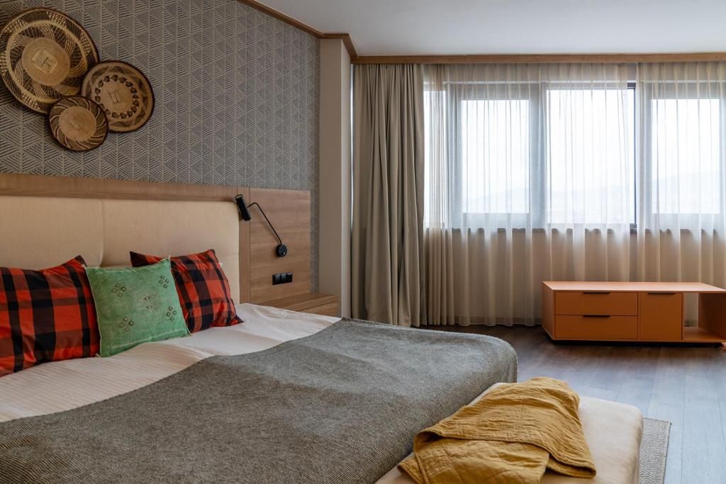 Una habitación de hotel con cama, mesita de noche, cómoda y ventana con cortinas.