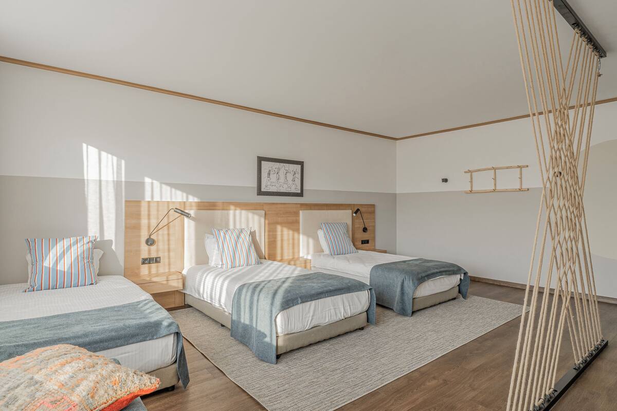 A modern bedroom with two beds, a wooden headboard, a hanging macrame, and a framed picture on the wall.