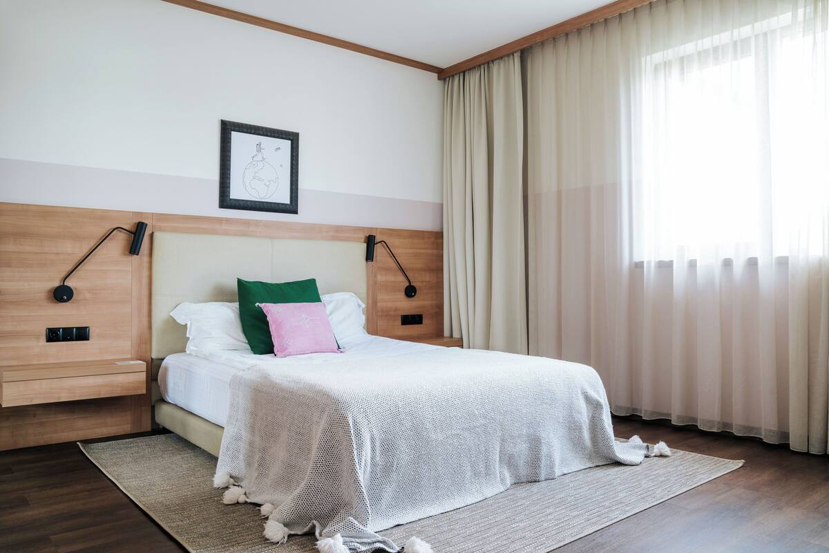A neatly arranged hotel room with a bed, a framed picture on the wall, and a window with curtains.