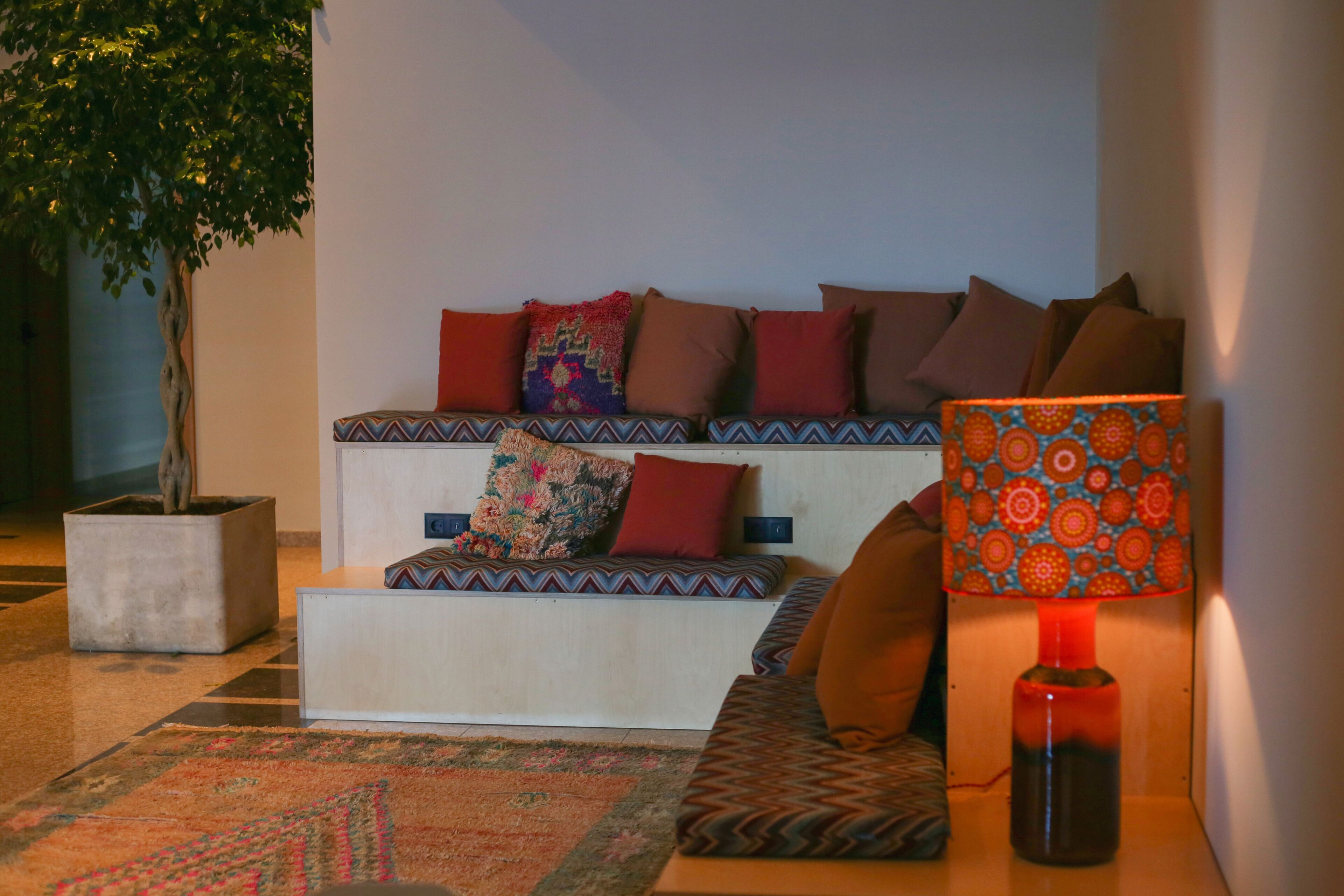 Un coin salon confortable avec un canapé, des coussins à motifs, une petite table et une lampe sur pied.