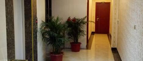 A hallway with marble flooring, potted plants, and a door at the end.