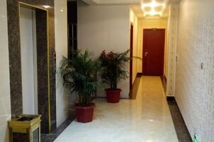 Un pasillo con suelo de mármol, plantas en macetas y una puerta al final.
