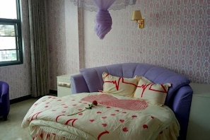 Un dormitorio con cama, mesita de noche, ventana y lámpara de pared.