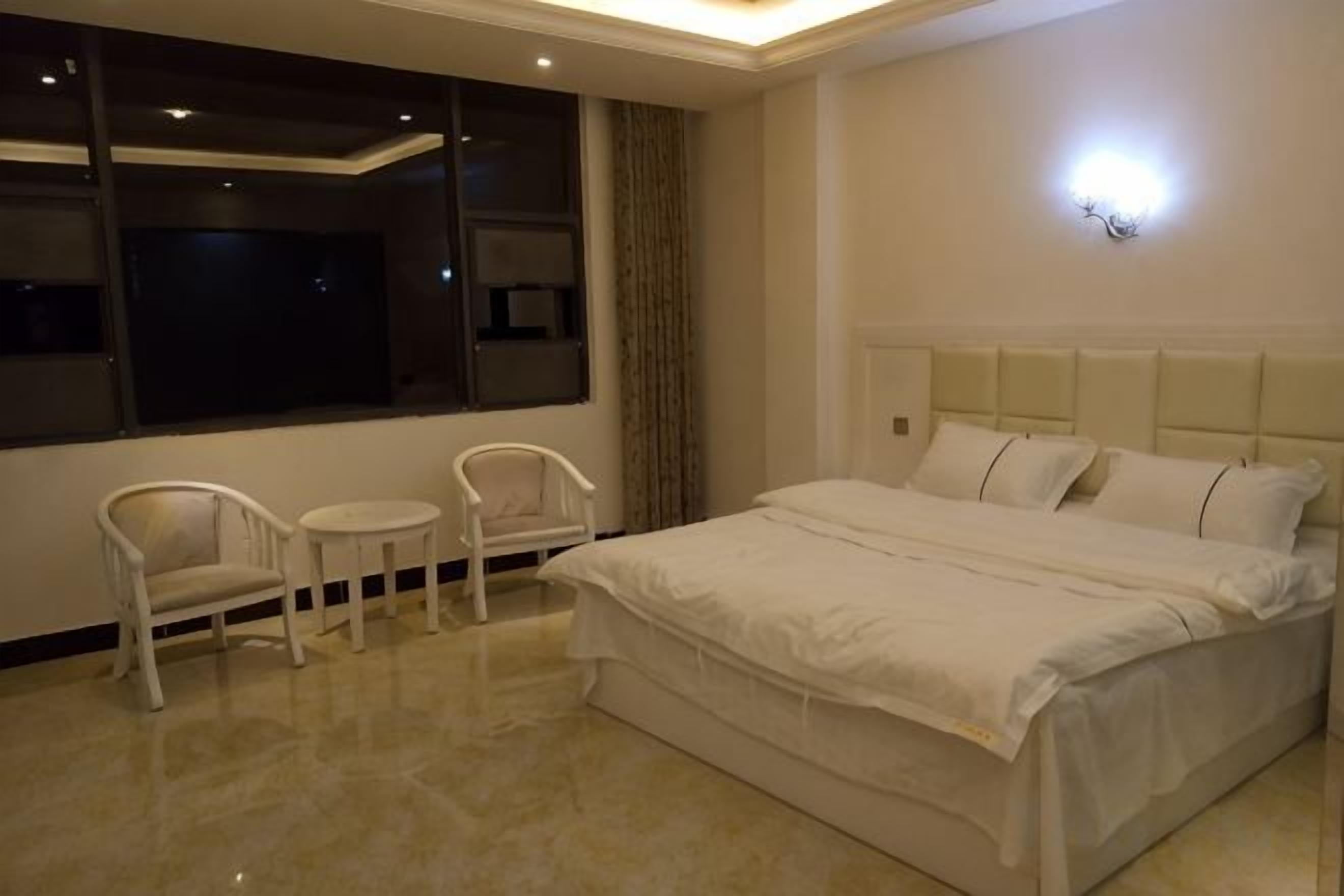 Een slaapkamer met een bed, twee stoelen, een klein tafeltje en een groot raam.