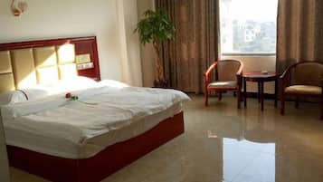 A hotel room with a bed, a chair, a table, and a potted plant.