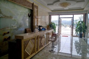 A reception area with a marble counter, bar stools, and a large potted plant. - Yuanmengyuan Hotel (Guangnan)