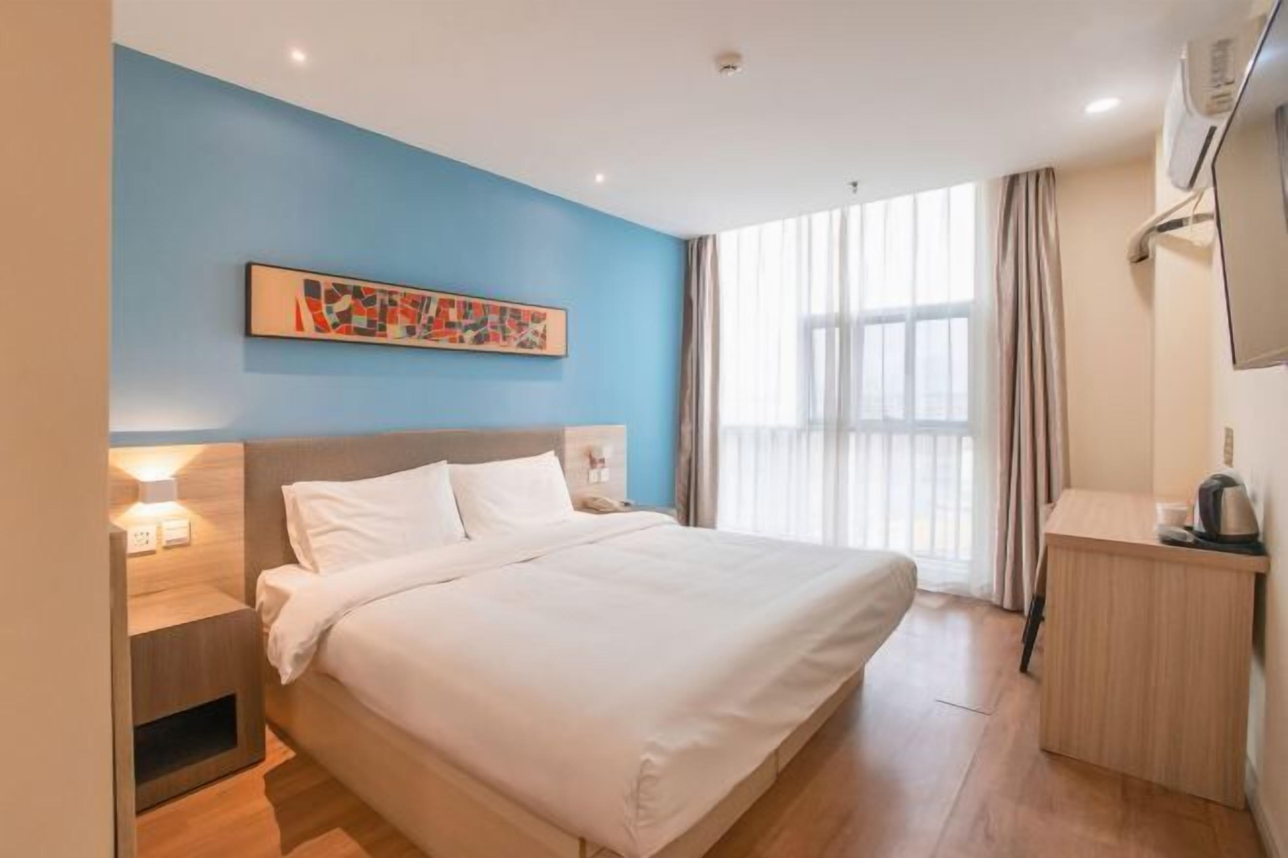 Ein Hotelzimmer mit Bett, Nachttisch, Lampe und einem Gemälde an der Wand.