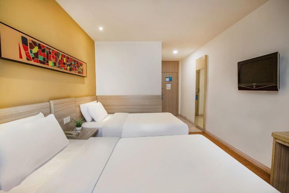 Een hotelkamer met twee bedden, een televisie en een schilderij aan de muur.