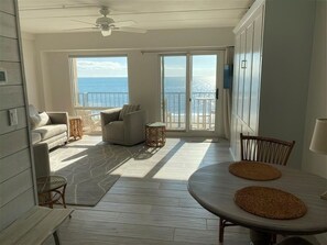Uma varanda espaçosa com vista para o mar, uma área de refeições com mesa e cadeiras, e uma área de estar com sofá e uma mesinha lateral.